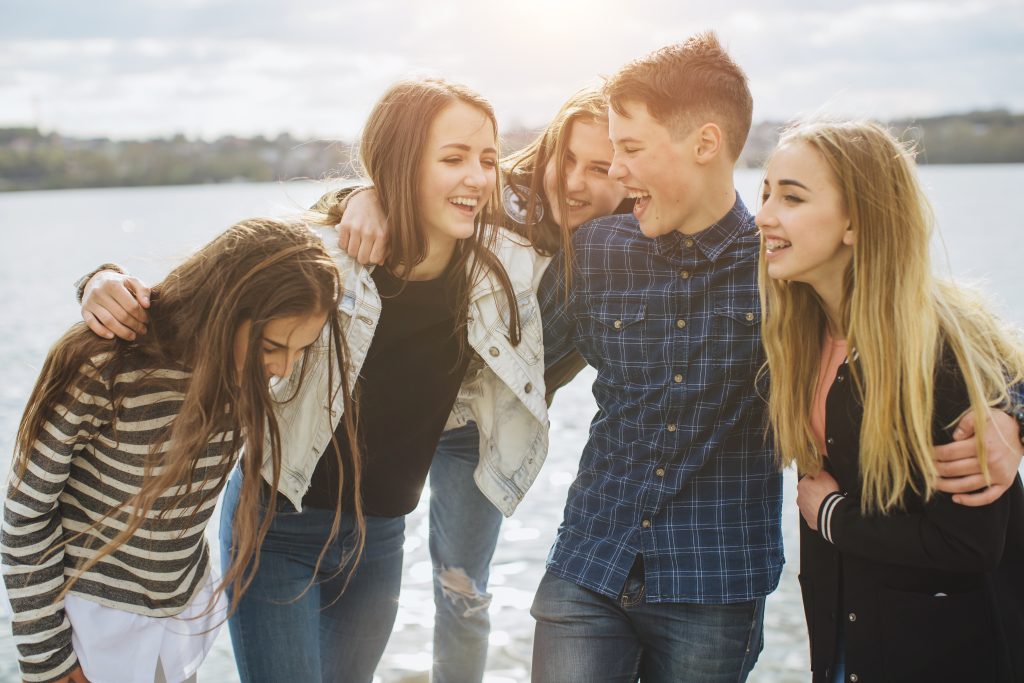 Summer holidays and teenage concept - group of smiling teenagers with skateboard hanging out outside.